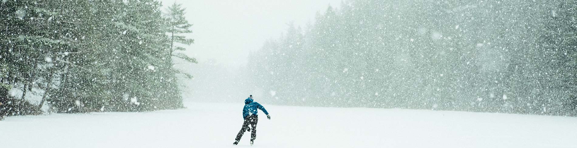 Person skating on a frozen lake while it snows.