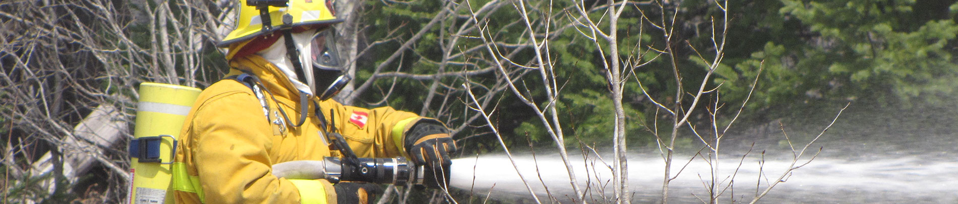 A Highlands East Volunteer Firefighter spraying his hose towards a fire.