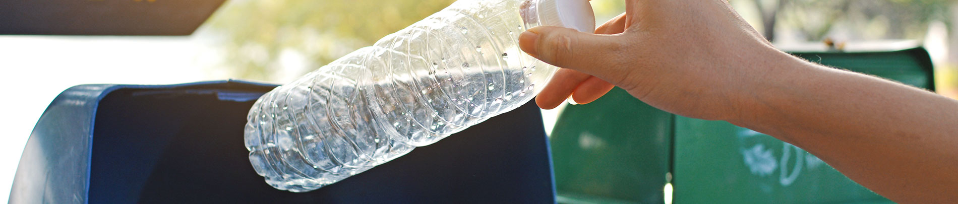 A close up of a person placing a water bottle into a recycling bin.